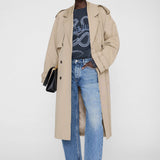 Person wearing a beige trench coat, graphic t-shirt, blue jeans, and black shoes on a white background